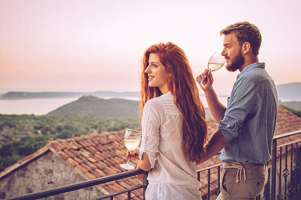 Couple sitting closely by river bank embracing at sunset with soft golden light reflection on water
